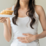 mulher segurando um prato com pães e com a mão na barriga representando o conteúdo sobre doença celíaca