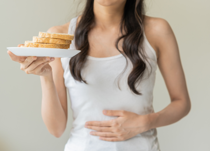 mulher segurando um prato com pães e com a mão na barriga representando o conteúdo sobre doença celíaca