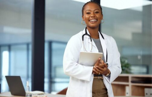 médica sorrindo, usando um jaleco, com um estetoscópio no pescoço e segurando um tablet