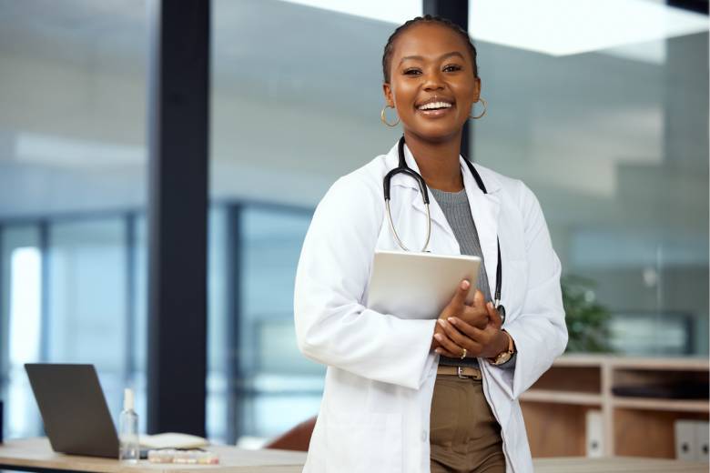 médica sorrindo, usando um jaleco, com um estetoscópio no pescoço e segurando um tablet
